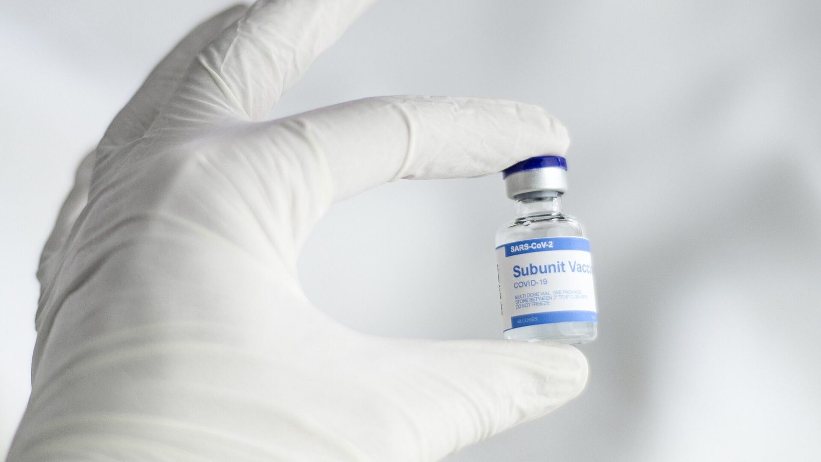 Vaccine vial held between gloved fingers